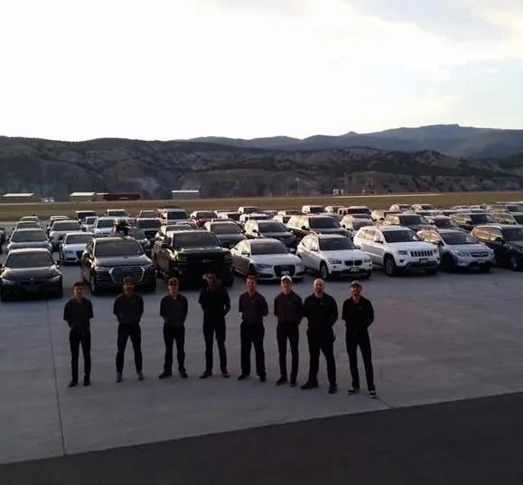 Valet team in black uniforms standing in front of rows of parked cars